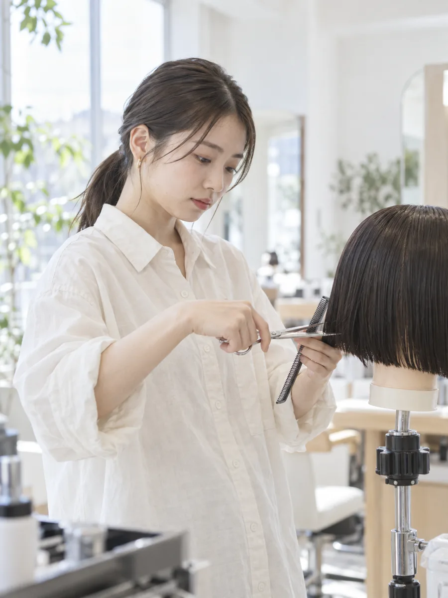明るいサロンでウィッグを使ってカットを練習するアシスタント